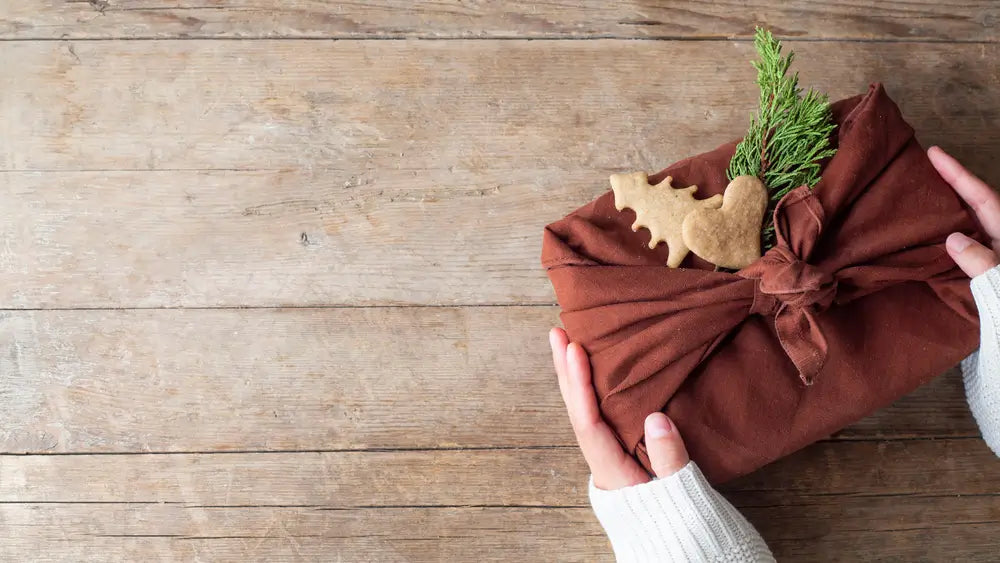 Hands holding a glass print gift wrapped in furoshiki style (reusable cloth).