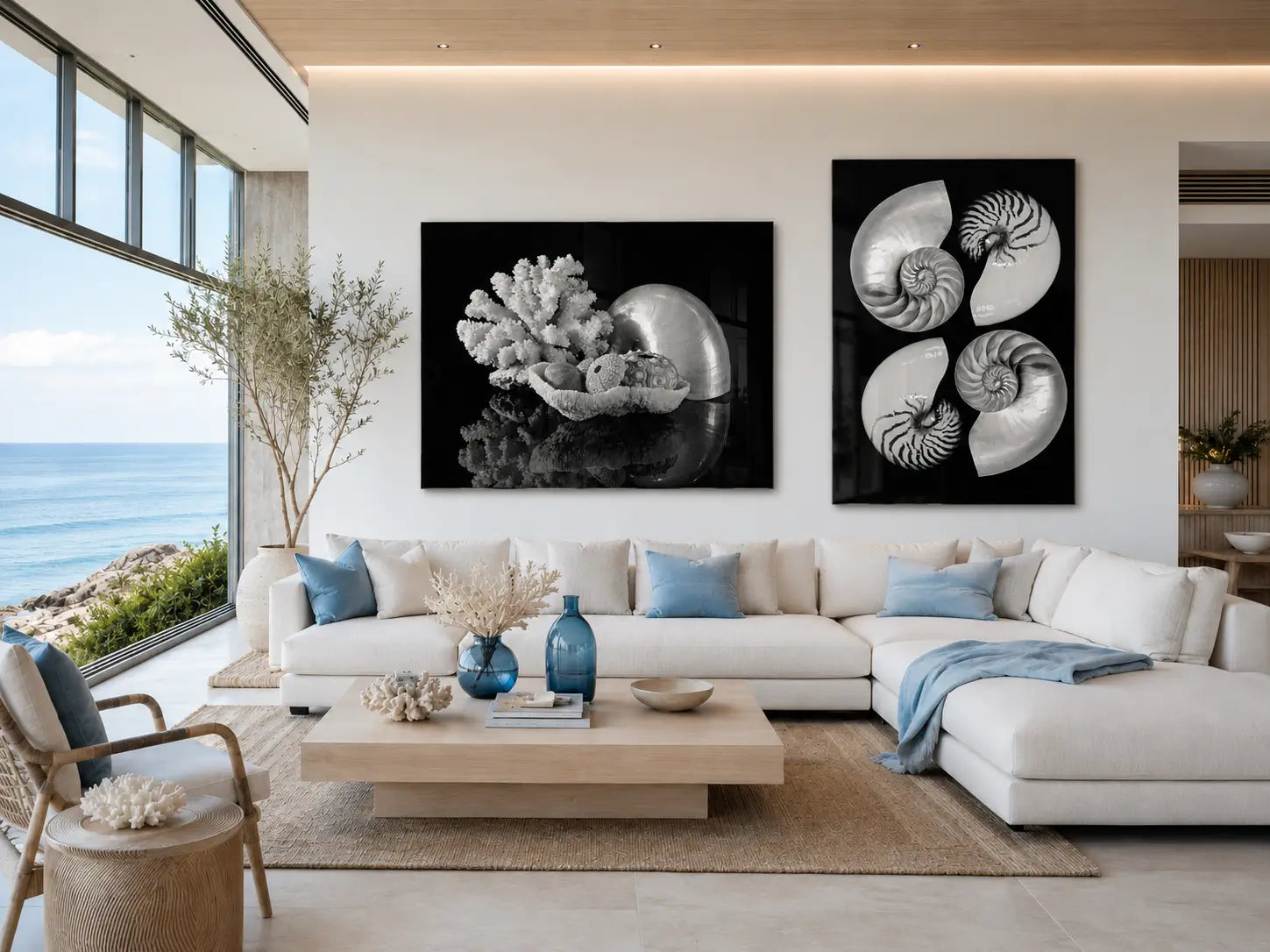 Ultra-modern coastal living room with ocean views, blue accents, and two black-and-white glass prints featuring nautilus shells, coral, and sea urchins displayed side by side above a white sectional sofa.