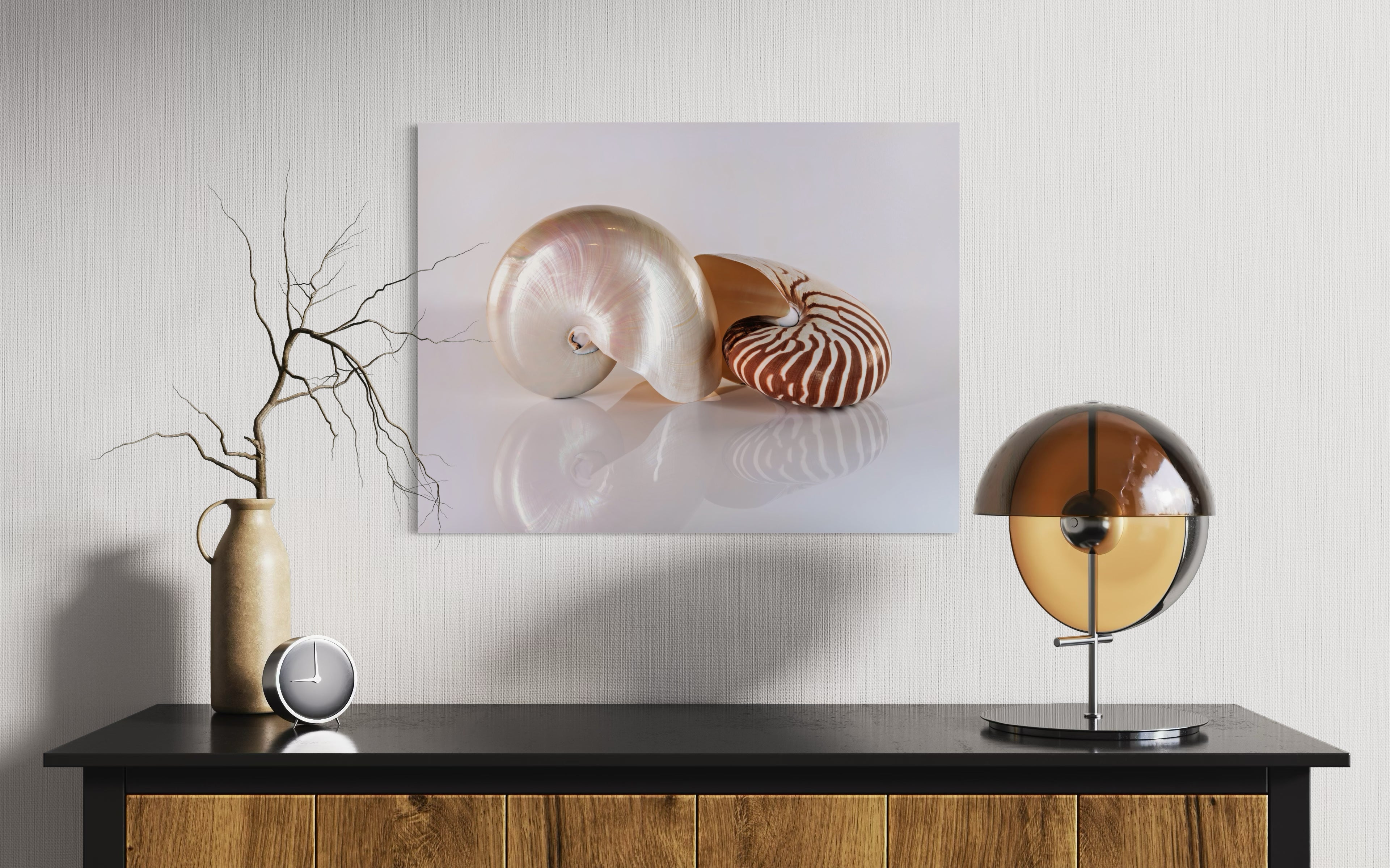 Modern wall decor: glass print of two chambered nautilus shells on reflective surface above wooden console with vase and lamp.