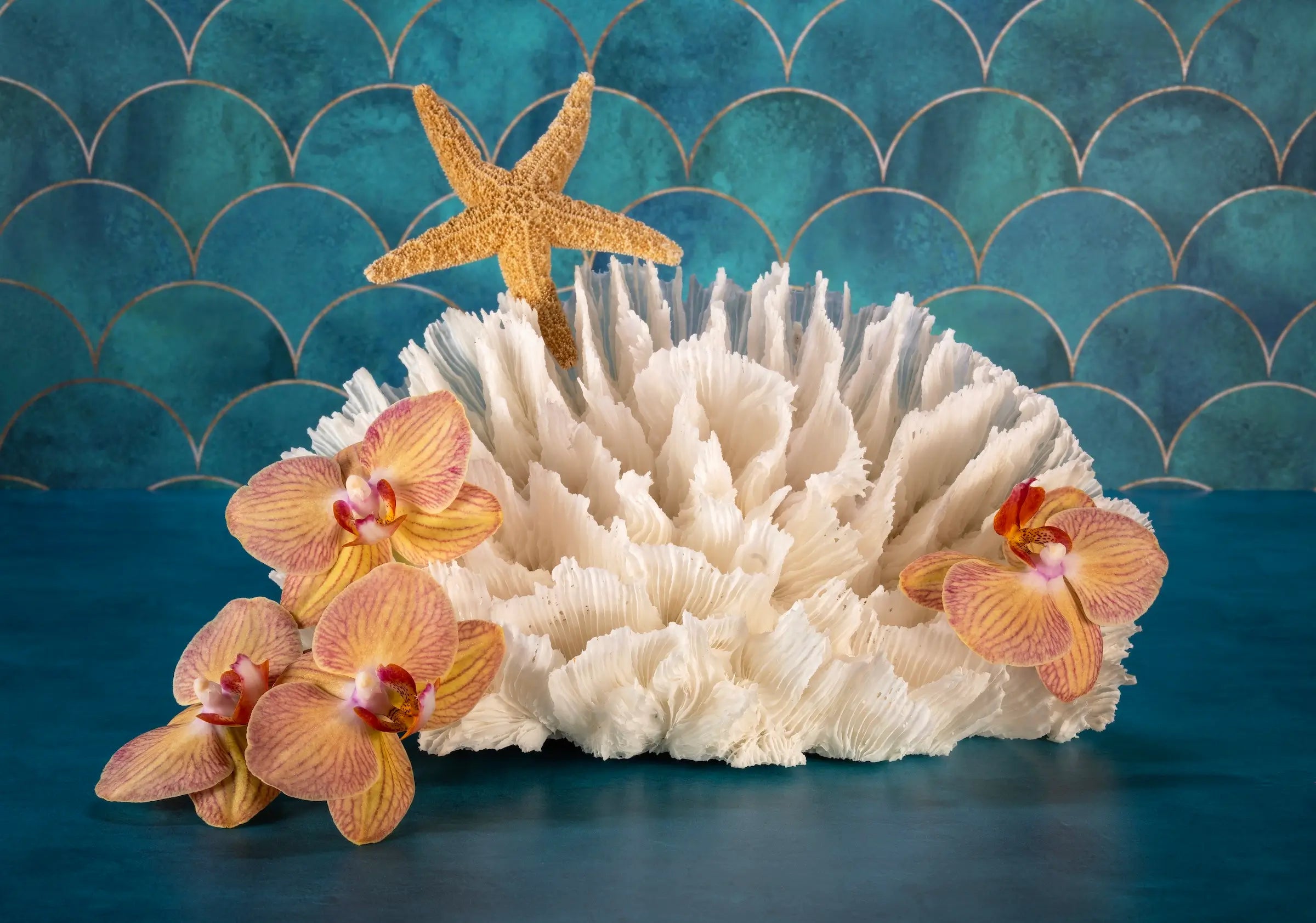 Vibrant tropical glass print of orchids, poca coral and a starfish on a colorful blue background that evokes the sea.