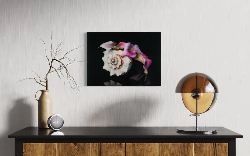 Pink calla lily and Triton’s Trumpet seashell on black coastal glass print, elegant botanical art above sideboard