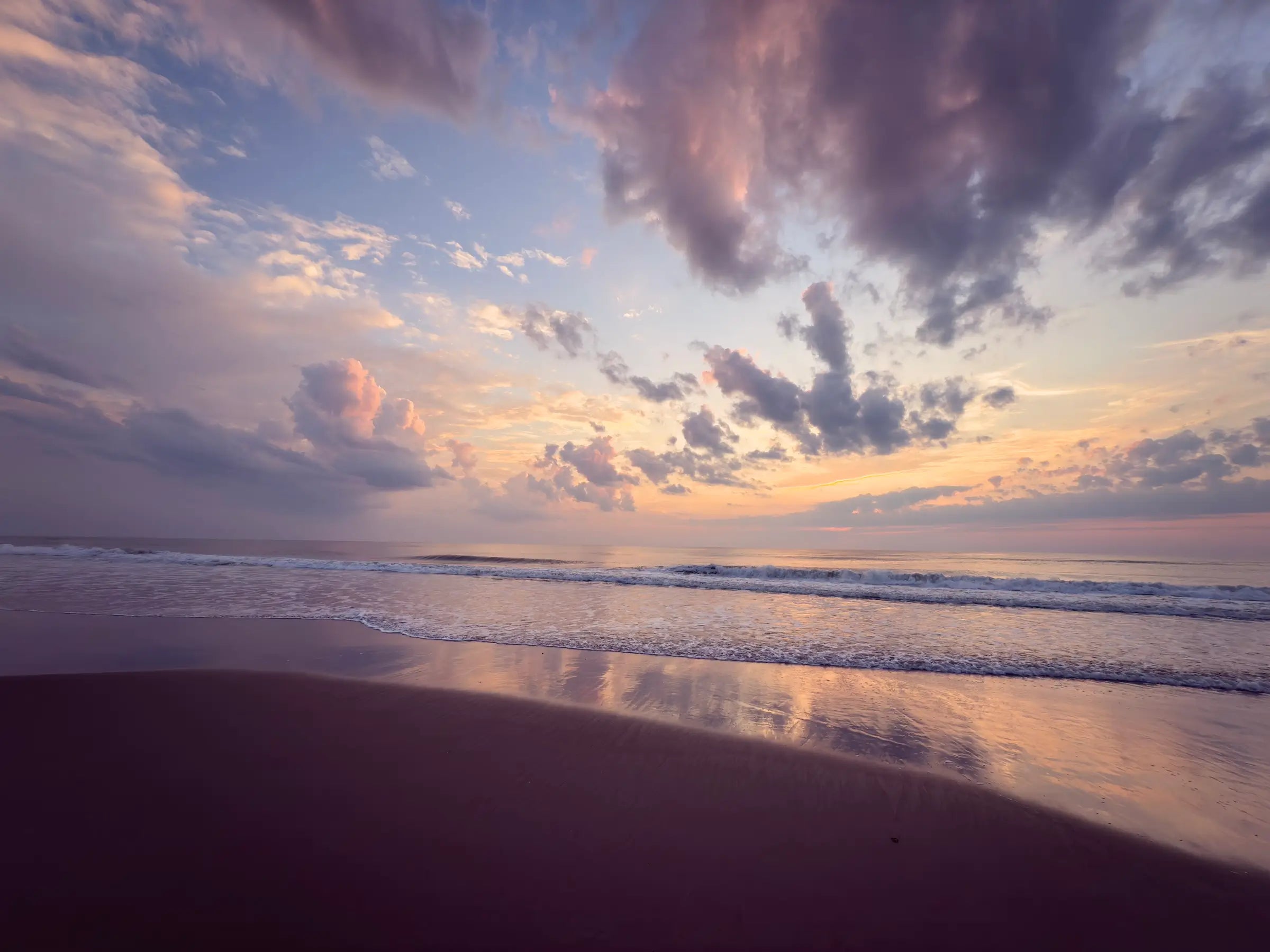 Vibrant coastal glass print featuring a sunrise on Corolla Beach in the Outer Banks, with the sun's colors reflecting on the wet sand and soft waves.