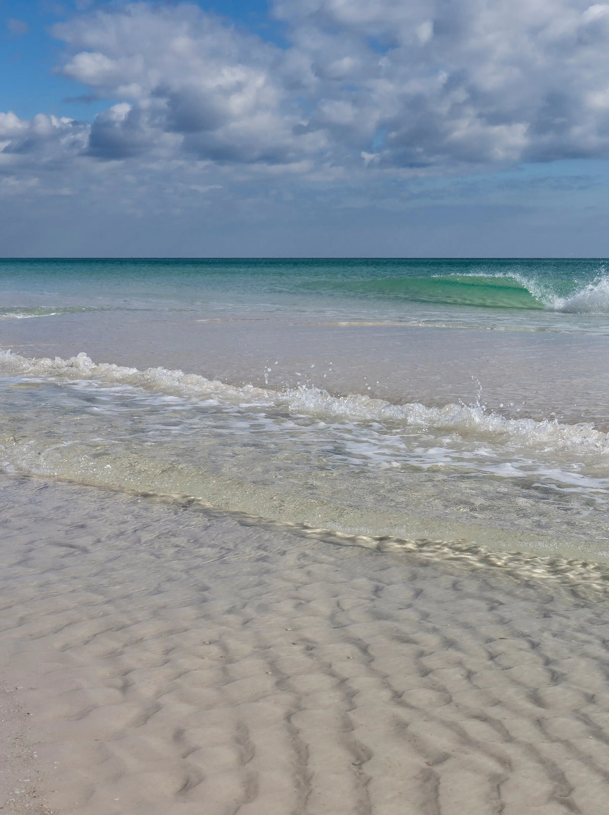 Center panel of Crystal Clear Beach Triptych showing clear turquoise Gulf water, rippled sand, gentle surf, and a cloudy blue sky