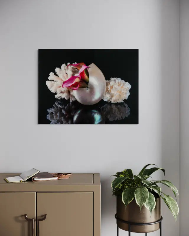 Coastal glass print of a pearl nautilus, coral and pink lilies on black reflective background for ocean wall art and coastal decor.