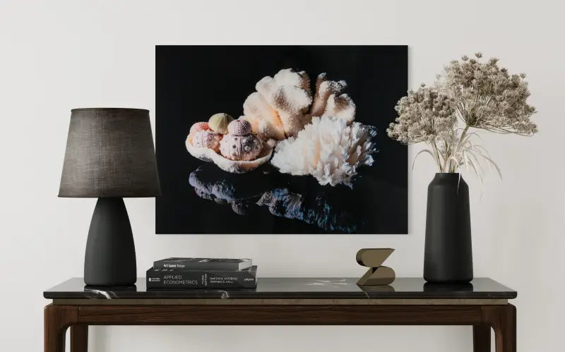 Glass print of white coral and sea urchins on black background above side table.