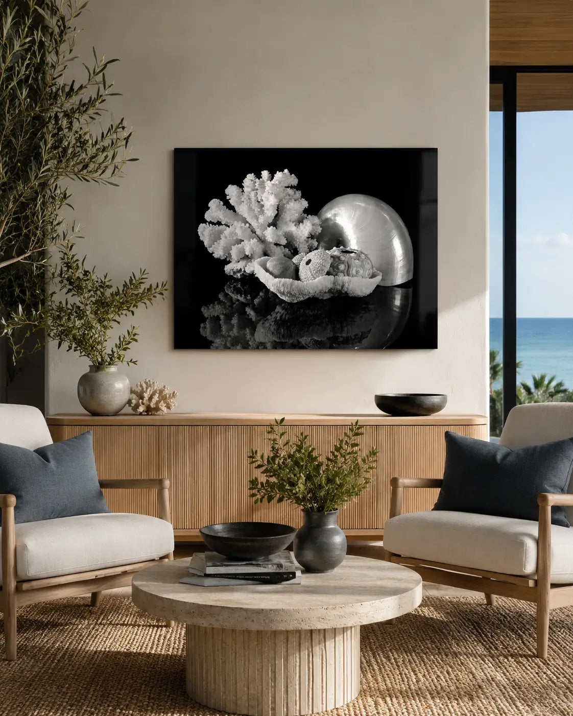 Black-and-white pearl nautilus, coral, and sea urchin glass wall art displayed in a warm modern coastal sitting area with charcoal accents and an ocean view.