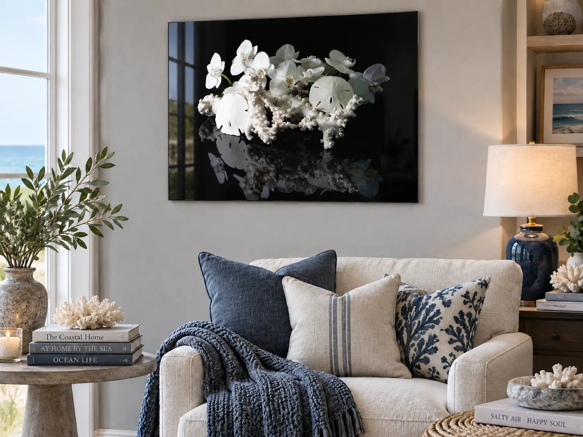 Sand dollar and coral coastal glass print displayed in a cozy coastal living room with blue and charcoal accents, showing the glossy frameless glass finish.