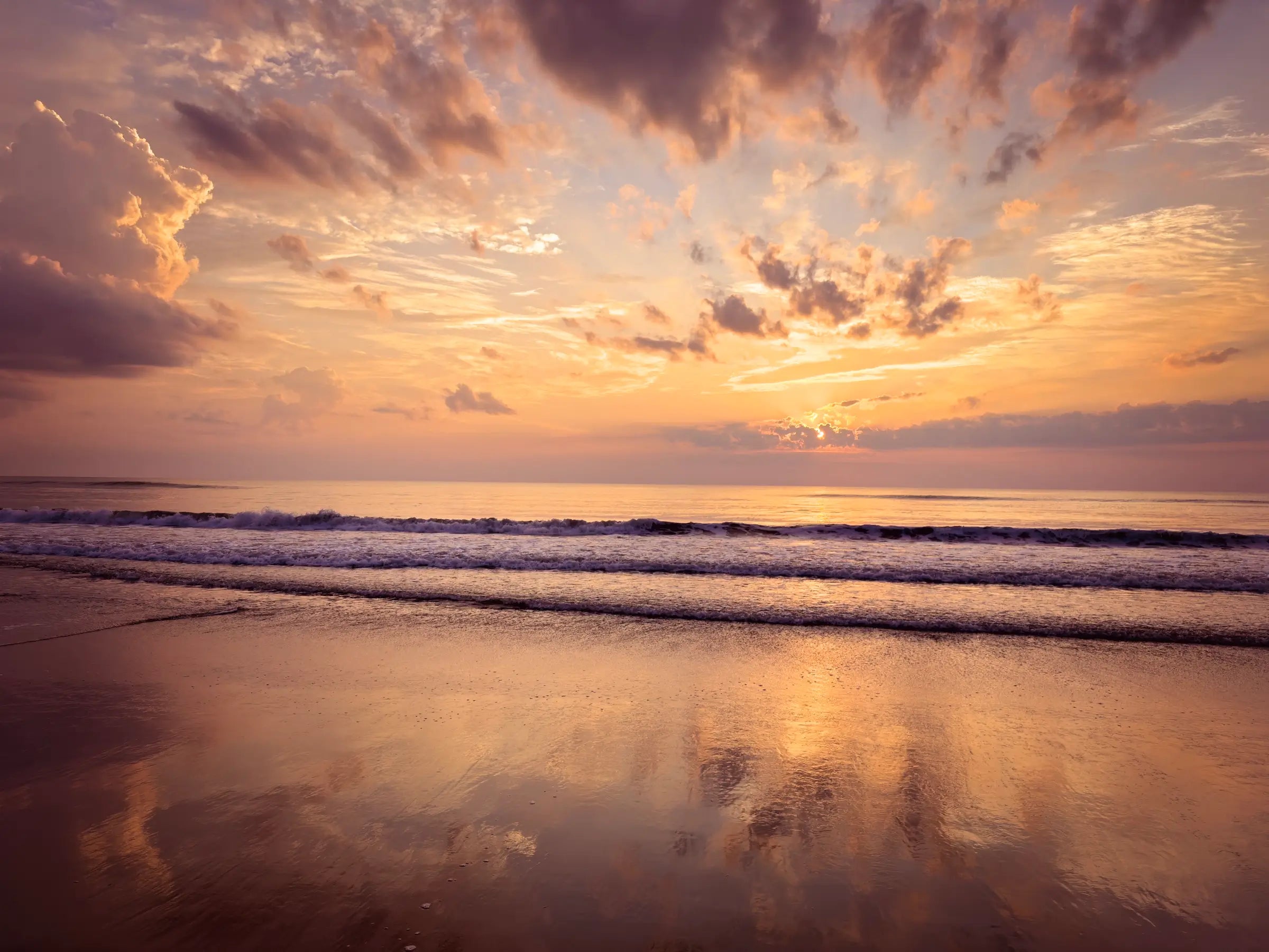 Vibrant coastal glass print featuring a sunrise on Corolla Beach in the Outer Banks, with golden light reflecting on the calm ocean waves and soft sand.