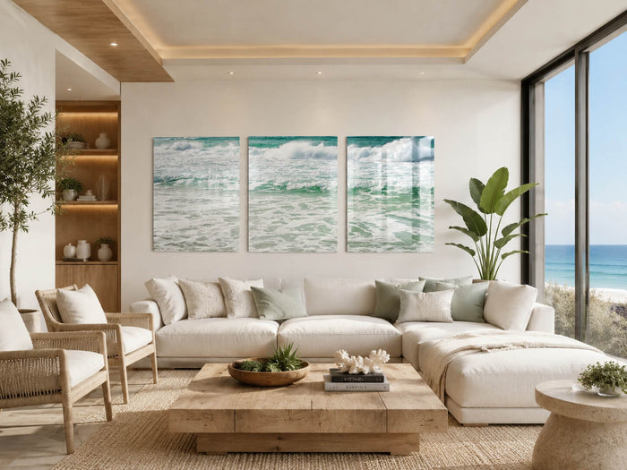 Ultra-modern coastal living room with sweeping ocean view, soft neutral furnishings, warm wood accents, and a wave triptych glass print above a cream sectional sofa.