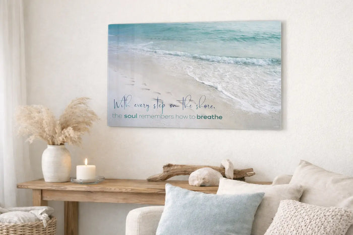 Serene coastal living room featuring a calming glass wall art print with ocean waves and the quote ‘With every step on the shore, the soul remembers how to breathe,’ symbolizing peace, calm, and coastal serenity for the new year.