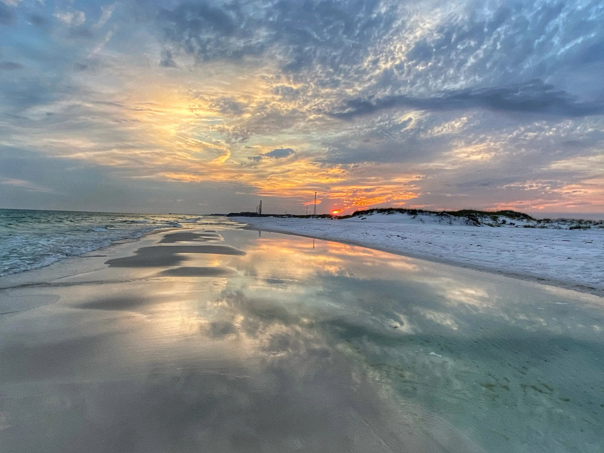 Reflective wet sand along a quiet shoreline mirroring clouds and soft coastal light.