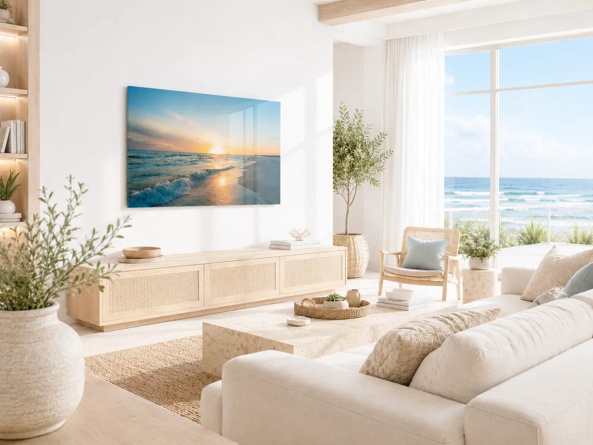 Light-filled coastal living room featuring a sunset beach glass print above a light wood console, with neutral furnishings, soft textures, and ocean views.