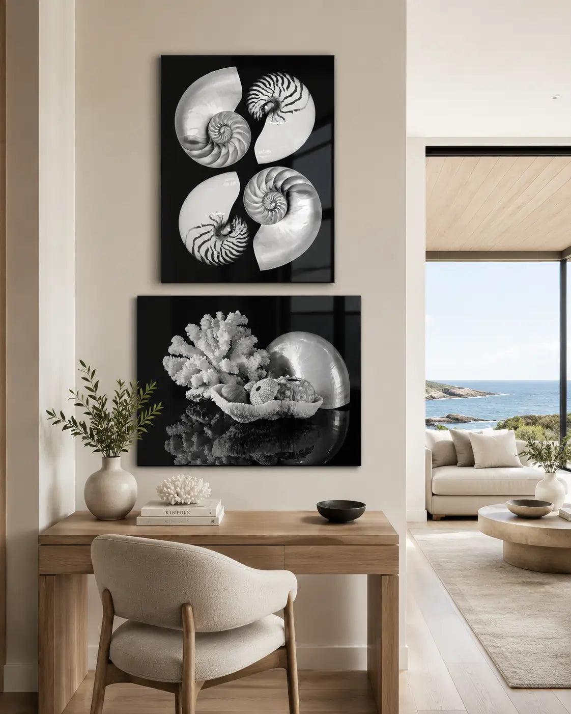 Two black-and-white nautilus and coral glass prints displayed above a warm neutral desk in a modern coastal home office with an ocean view.