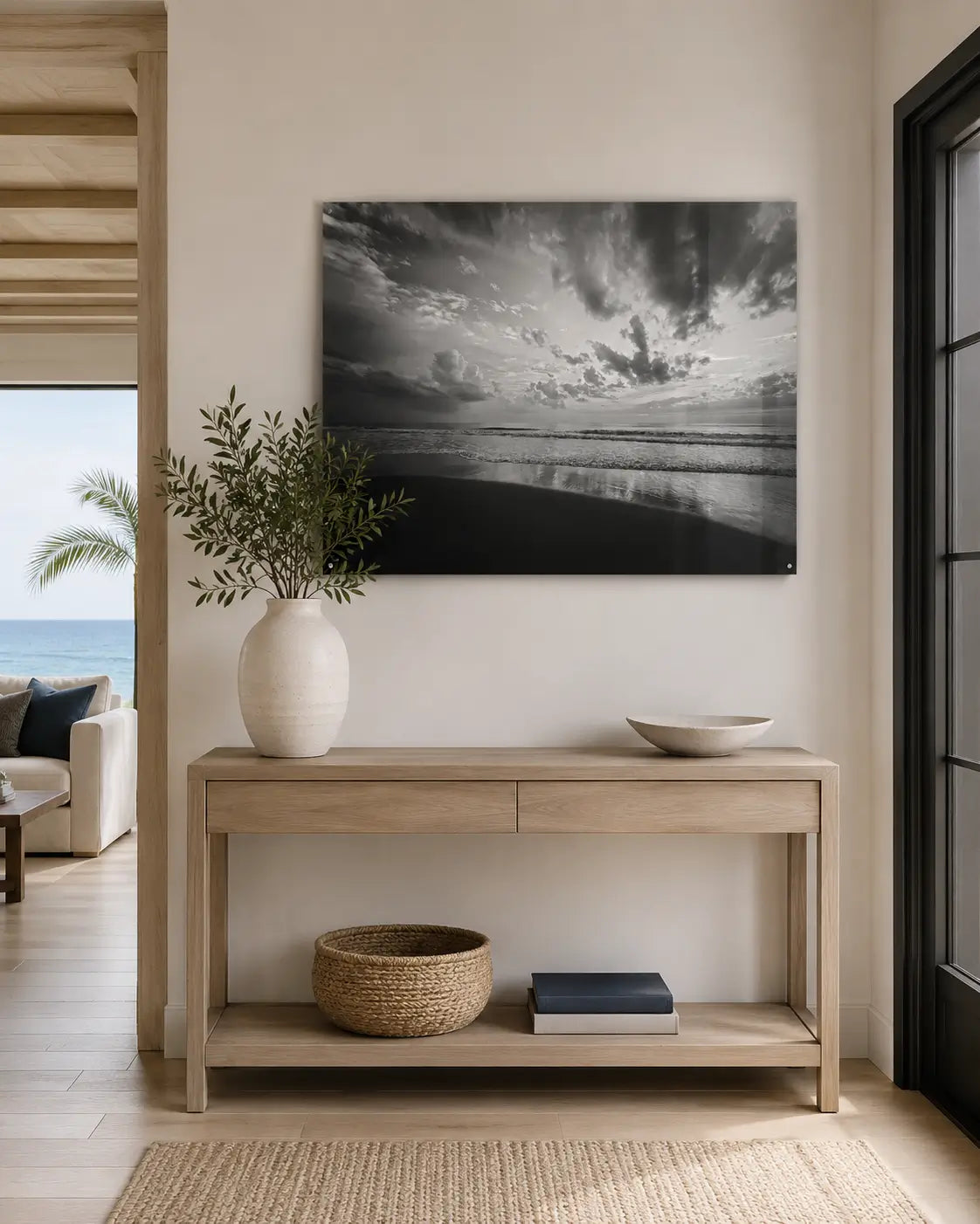 Black-and-white Corolla Beach sunrise glass wall art displayed above a light wood console in a warm modern coastal entryway.