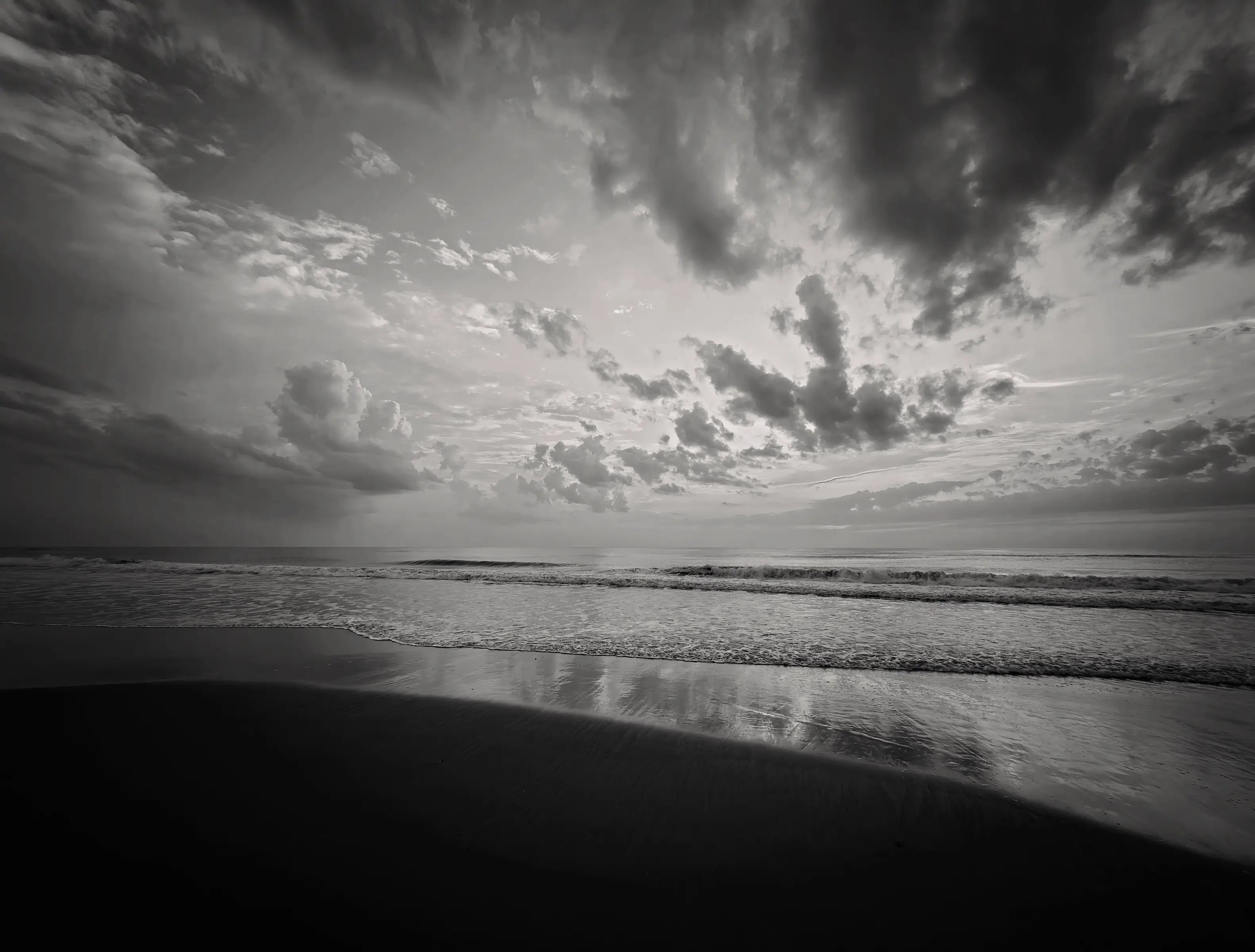 Black-and-white beach wall art showing layered clouds, rolling ocean waves, and reflections on wet sand at Corolla Beach.