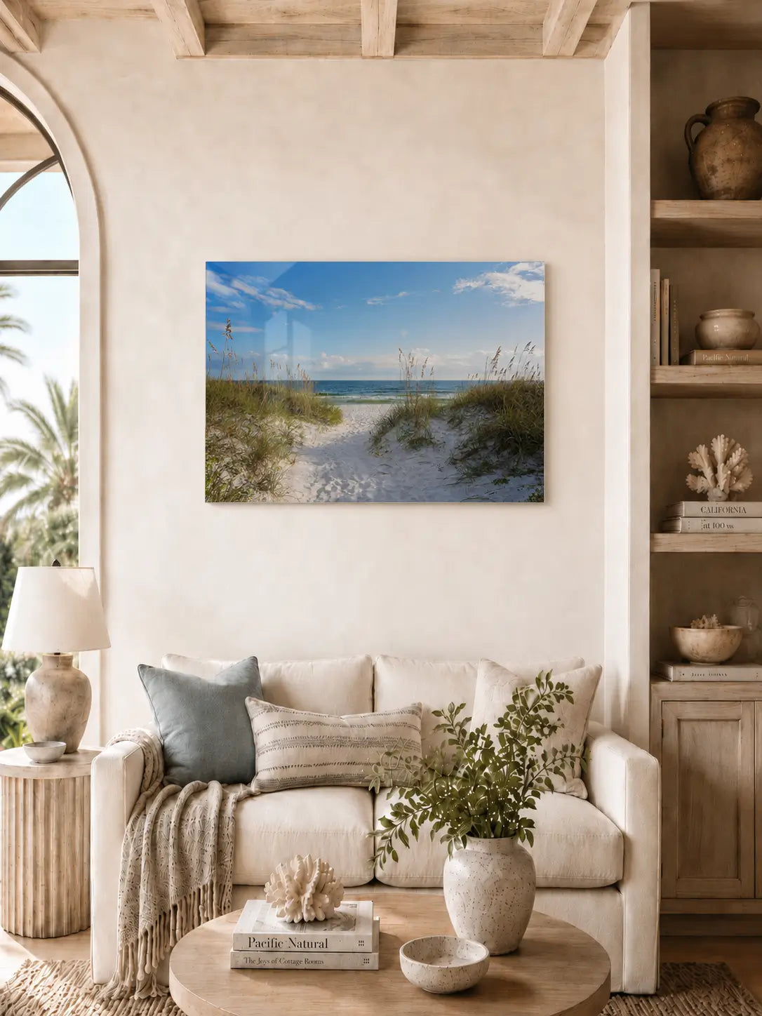Coastal living room with a beach scene glass print on the wall above a beige sofa.