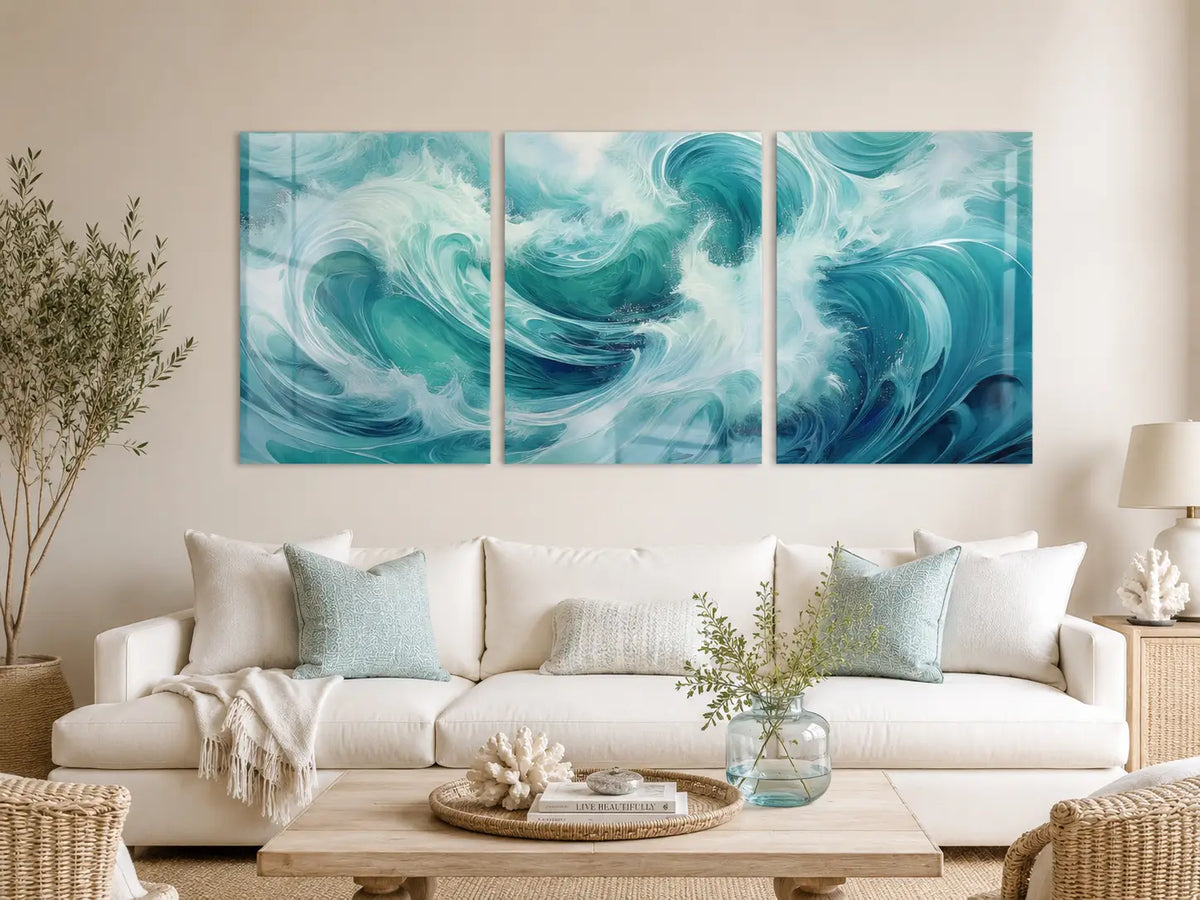 Ocean wave triptych glass wall art displayed above a white sofa in a light modern coastal living room with aqua accents.
