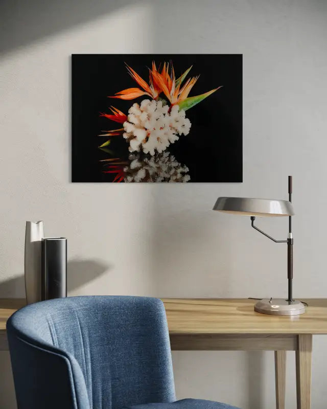 A glass print featuring bird of paradise flowers and coral on a black reflective background-above a desk.