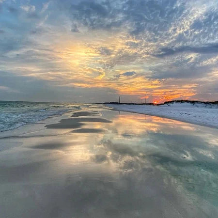 Sunset over a beach with clouds reflecting on the water