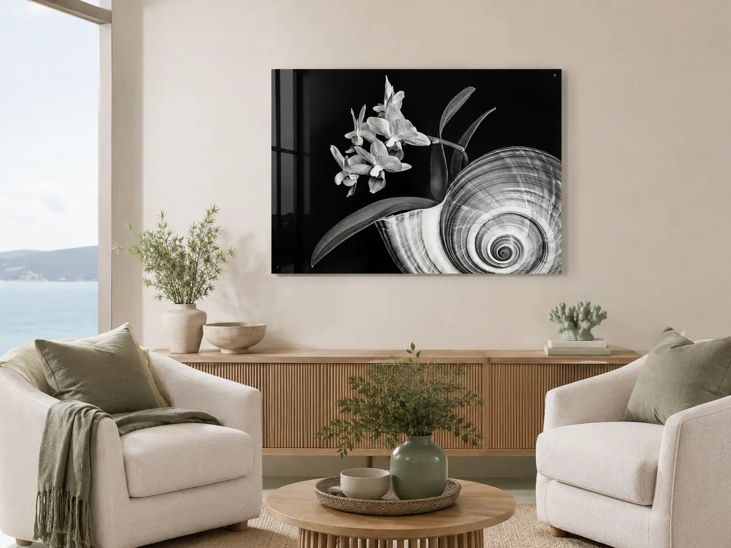 Black-and-white orchid and Giant Tun Shell glass wall art displayed in a warm modern coastal sitting area with sage accents and an ocean view.